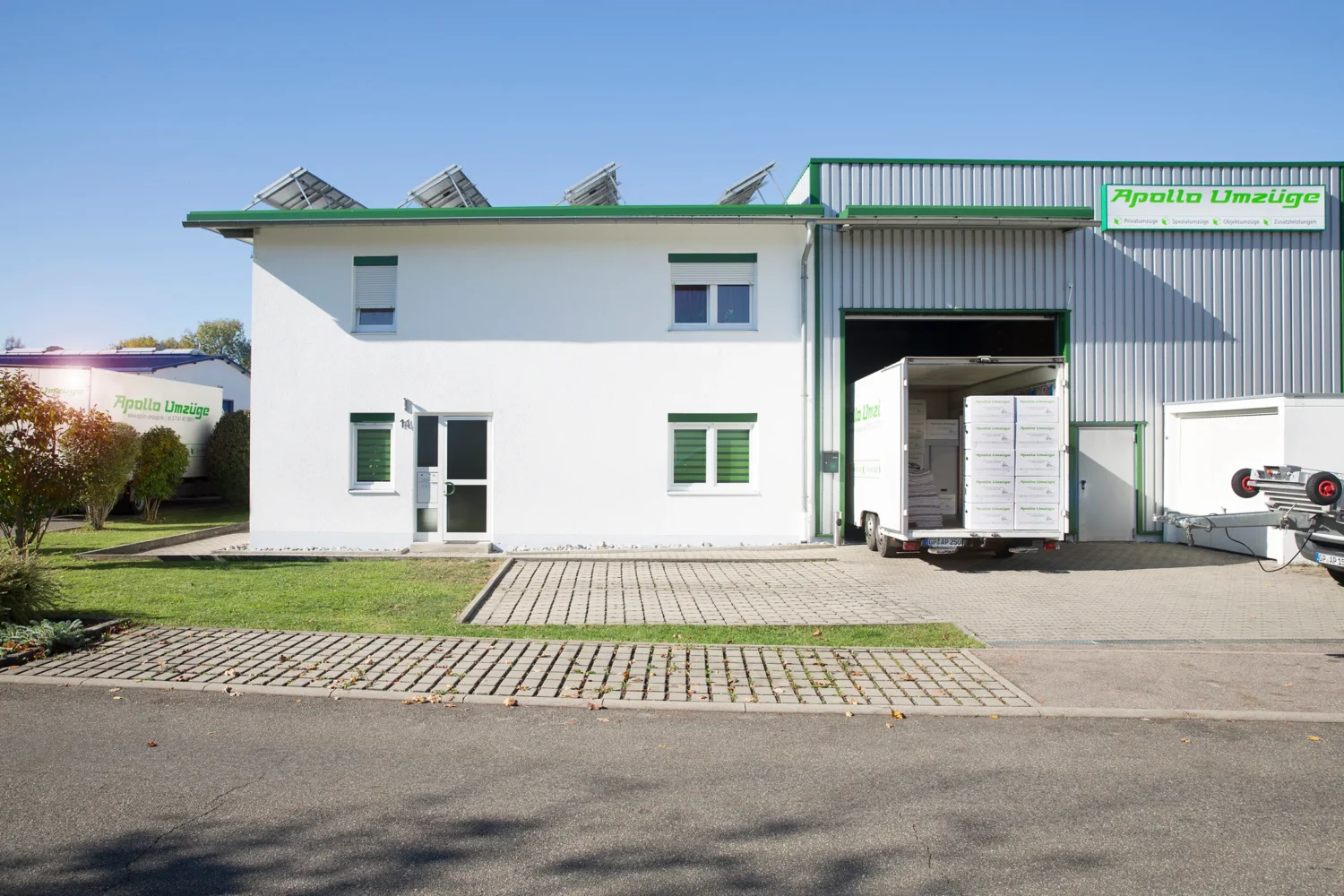 Gebäude mit Lagerhalle und LKW vor der Einfahrt an einem sonnigen Tag.