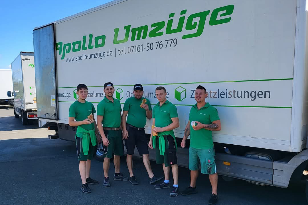 Fünf Männer in grüner Arbeitskleidung stehen vor einem Umzugs-Lkw mit der Aufschrift Apollo Umzüge.