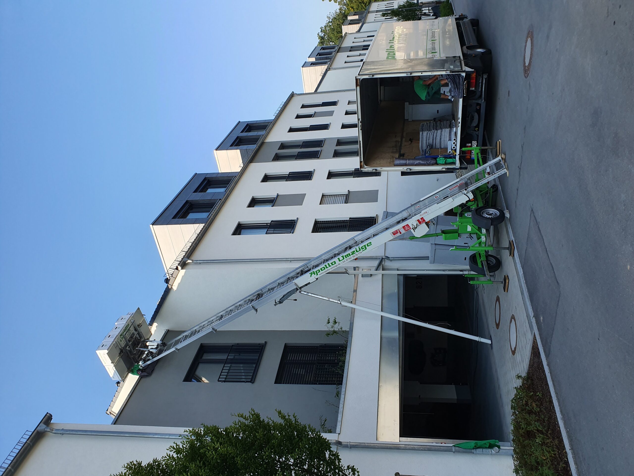 Umzugshelfer transportieren Möbel über eine lange Treppe an der Fassade eines modernen Wohngebäudes.