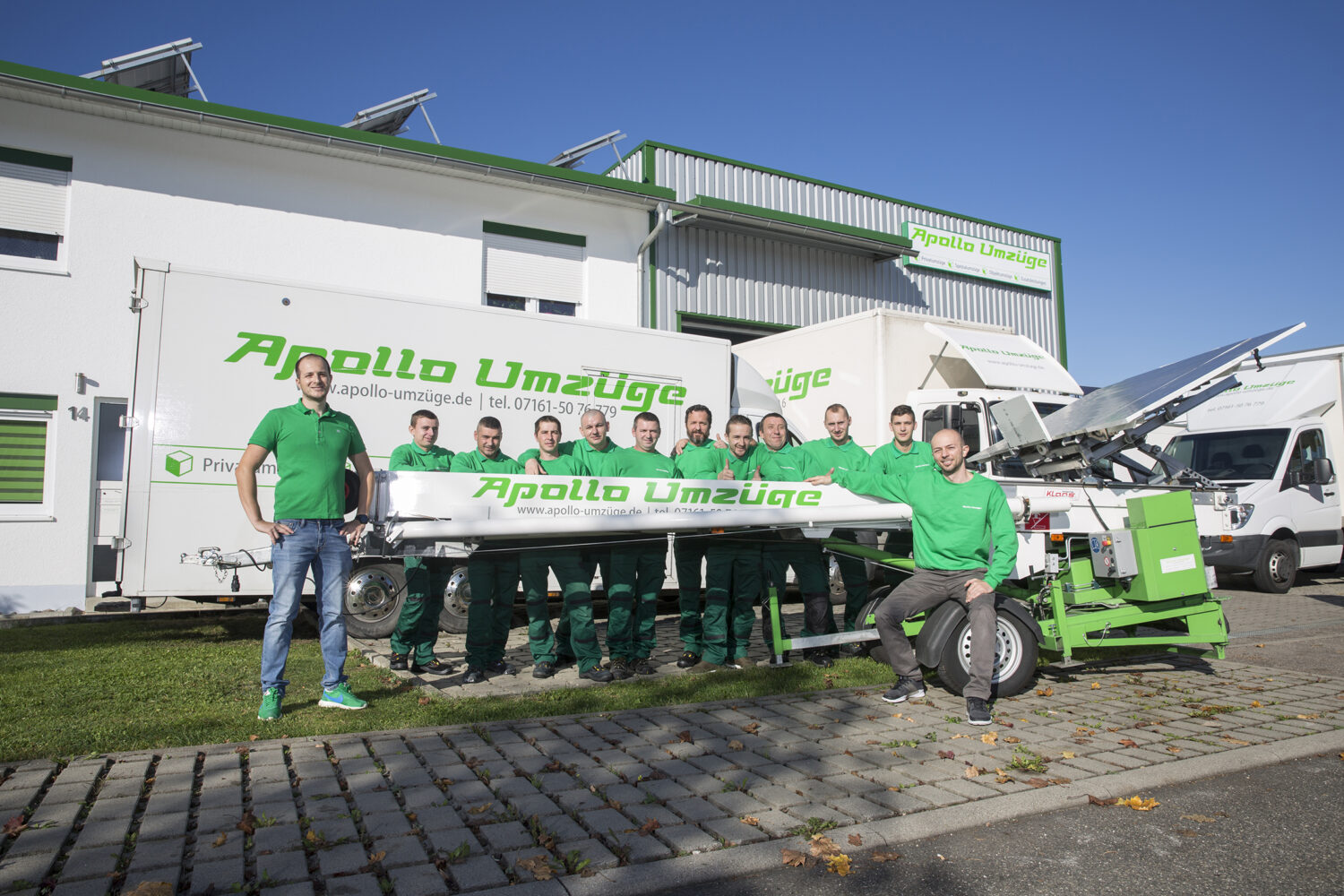 Team von Umzugshelfern in grünen Shirts vor Umzugsfahrzeugen mit Banner Apollo Umzüge.