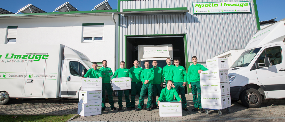 Team von sieben Personen in grüner Arbeitskleidung vor zwei weißen Lieferwagen und einem Gebäude mit dem Schriftzug "PiperLO Umzüge".