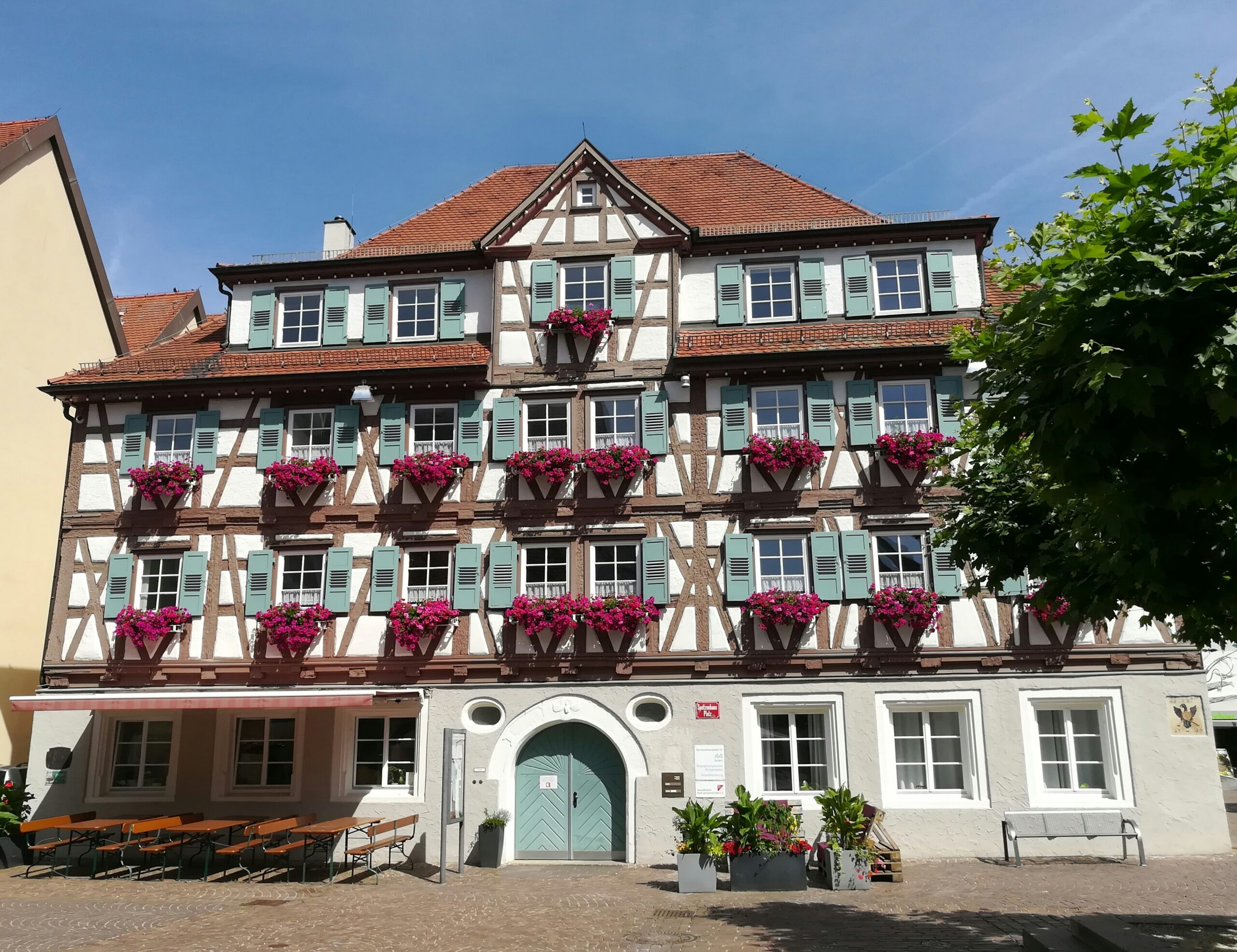 Fachwerkhaus mit roten Dachziegeln und Blumenkästen an den Fenstern bei klarem Himmel.