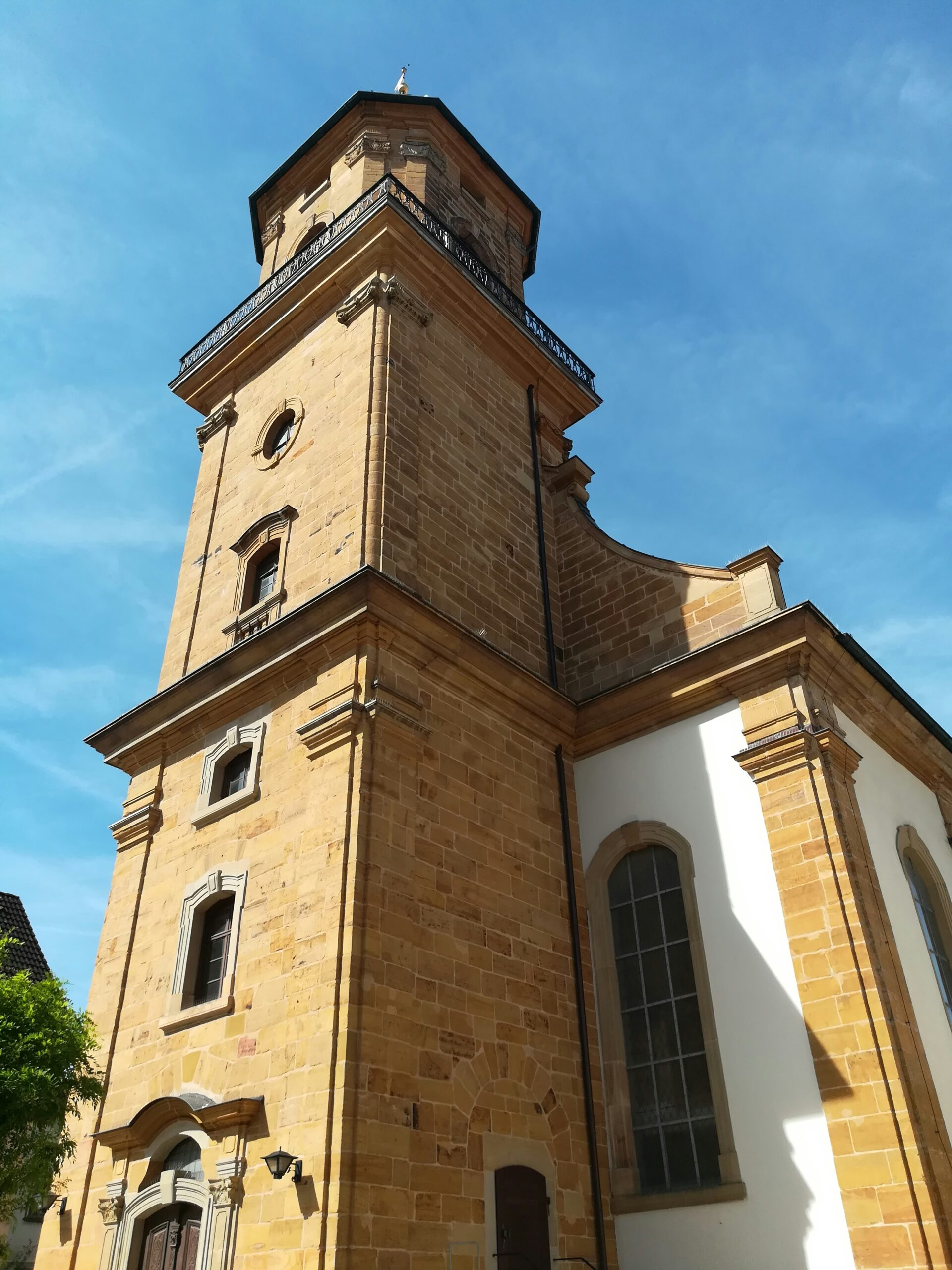 Kirchturm aus gelbem Stein vor blauem Himmel, Blick von unten.