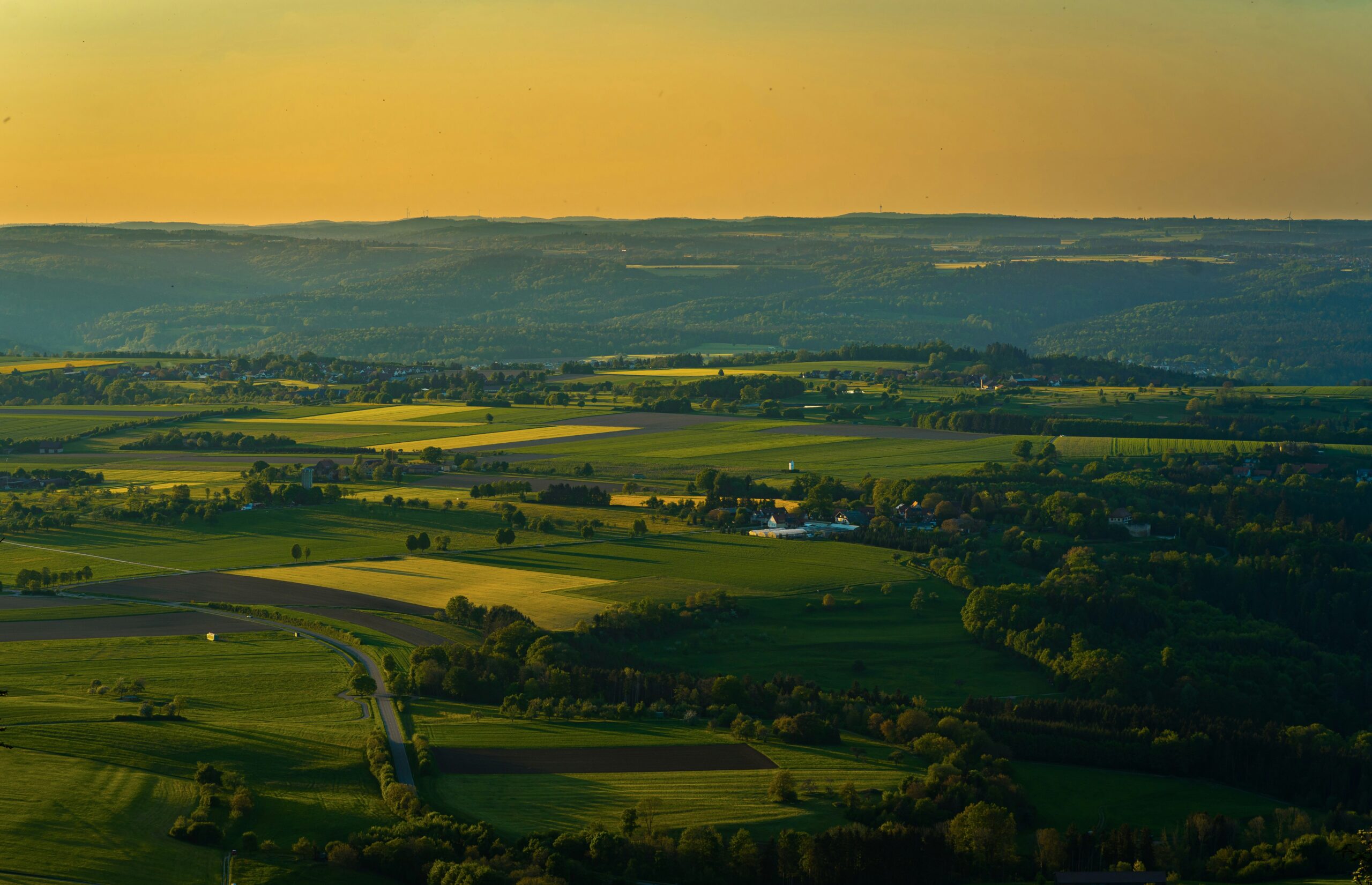 Landschaft mit Feldern, Wäldern und Hügeln bei Sonnenuntergang.