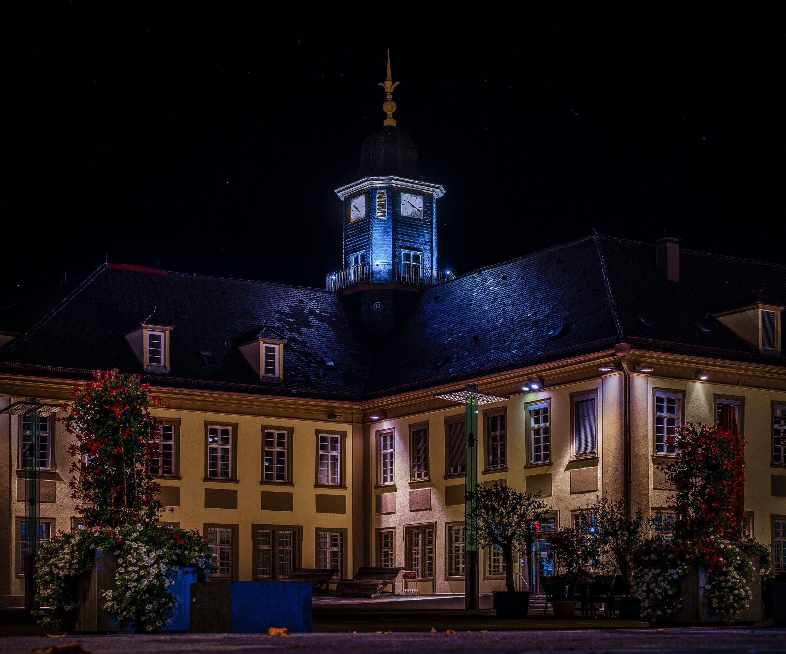 Beleuchtetes historisches Gebäude mit Uhrenturm bei Nacht.