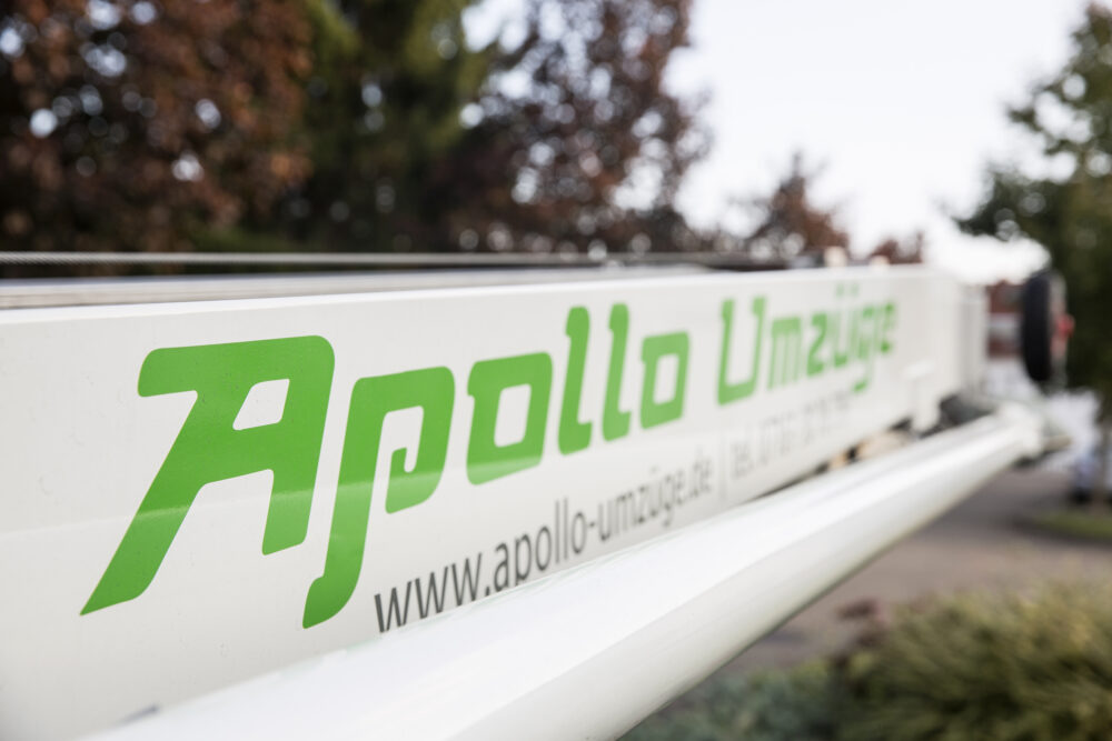 Nahaufnahme eines weißen Fahrzeugs mit grünem Schriftzug Apollo Umzüge und einer Website-Adresse.