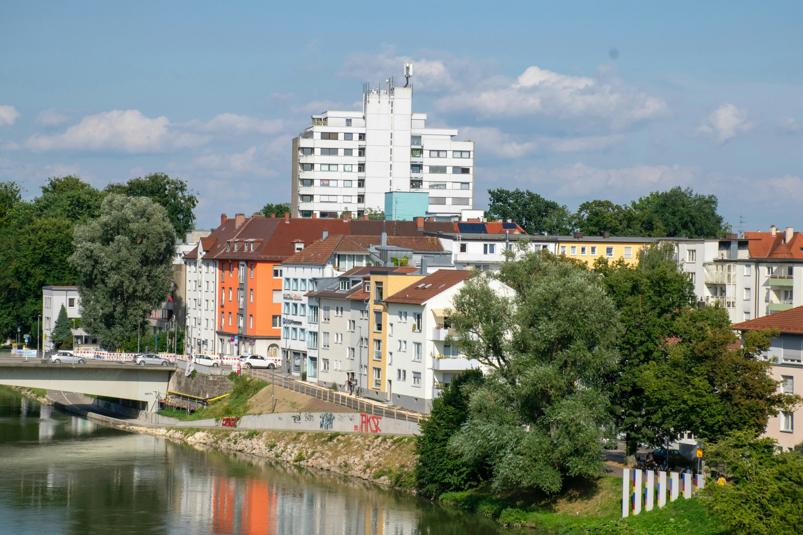 Stadtansicht mit bunten Wohngebäuden, Fluss und Brücke bei klarem Himmel.